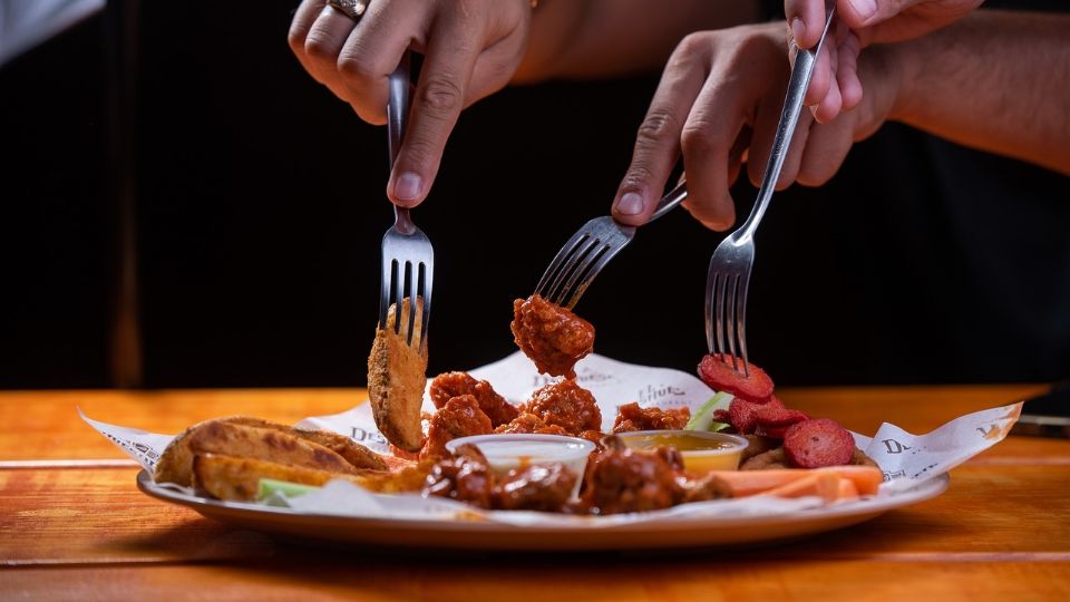 Un grupo de personas comparte un plato de alitas con sus respectivos complementos