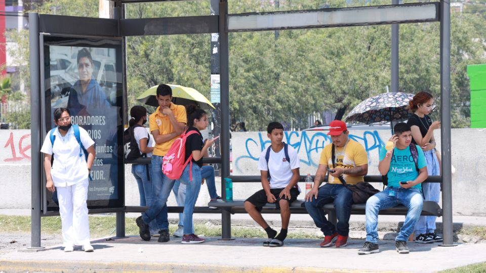 Personas en Monterreyse cubren de los rayos del sol abajo de una parada de camiones.