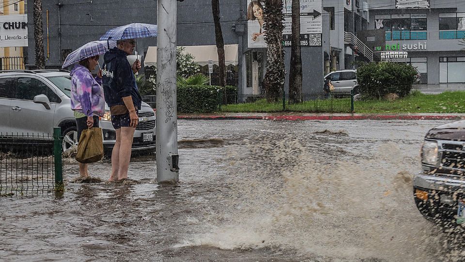 Una pareja sale de compras por una calle inundada tras el paso de la tormenta Hilary en la ciudad de Tijuana.