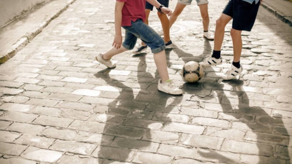 Fotografía ilustrativa de un grupo de menores de edad jugando futbol en la calle