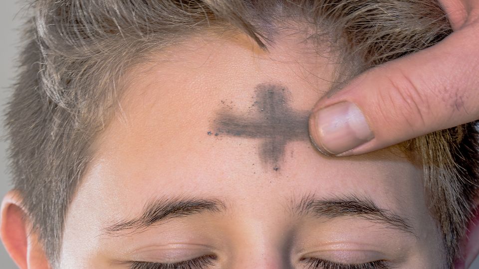 Padre coloca la ceniza en la frente de un niño tras el inicio de la Cuaresma