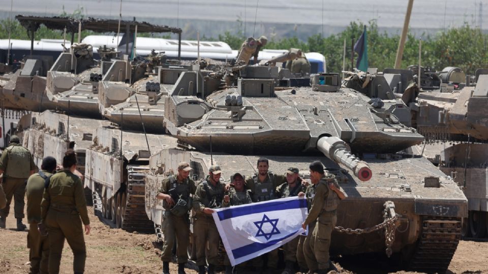 Un grupo de soldados israelíes sostiene una bandera israelí mientras se reúnen con vehículos militares en una posición no revelada cerca de la valla fronteriza con la Franja de Gaza, en el sur de Israel, el 9 de mayo de 2024.