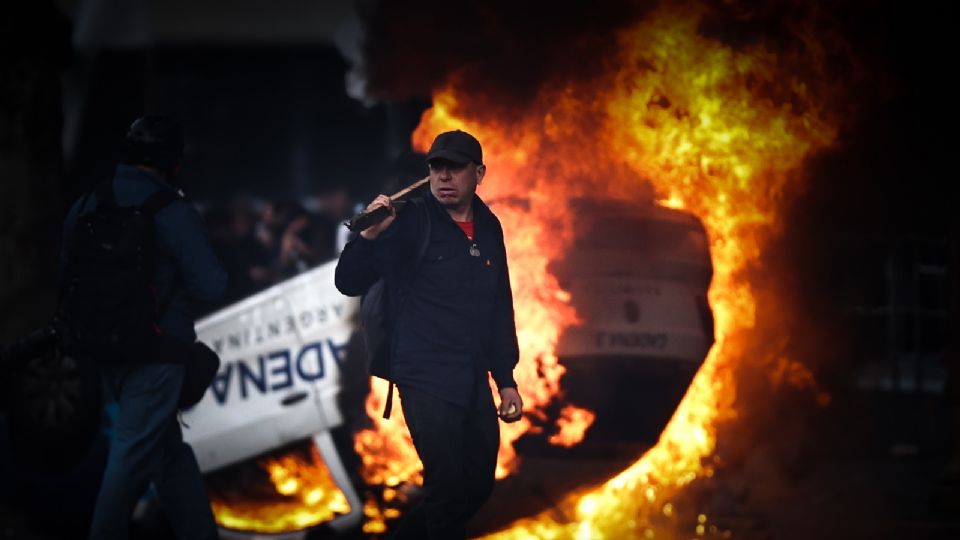 Un hombre es visto caminar frente a una carro en llamas en una protesta a las afueras del senado durante un debate de ayer miércoles, en Buenos Aires (Argentina).