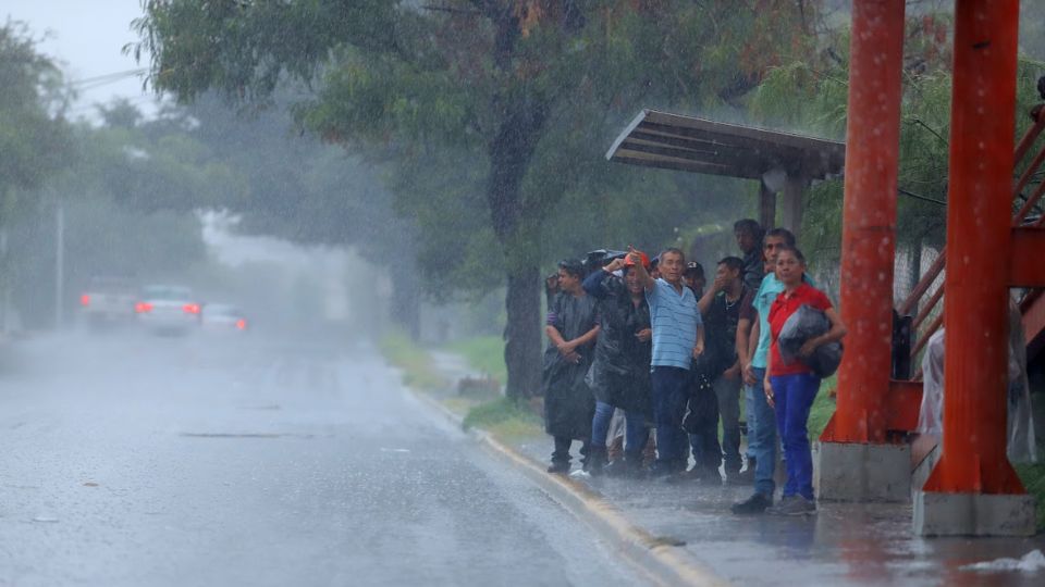 Personas esperan el camión debajo de la lluvia