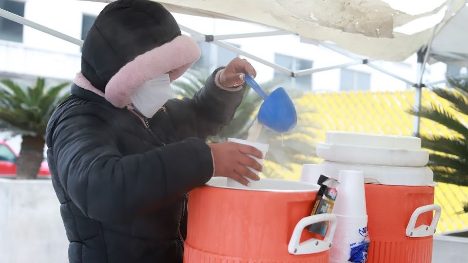 Persona se cubre del frío con cubrebocas y guantes, mientras reparte bebidas calientes en Monterrey ante bajas temperaturas.