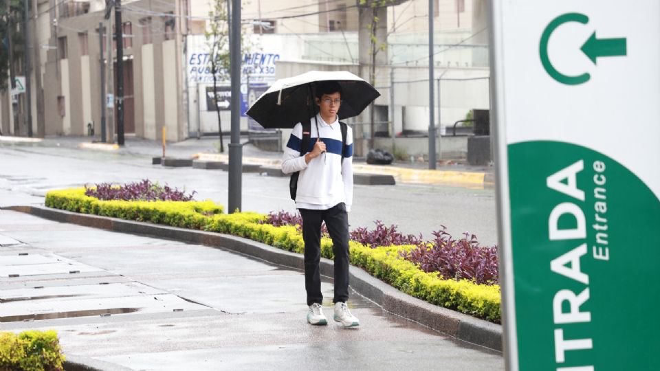 Joven usa paraguas para cubrirse de la lluvia que azota a Nuevo León