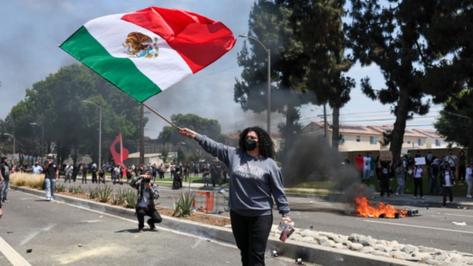 Mujer ondea la bandera de México durante protesta contra las redadas migratorias en Los Ángeles.